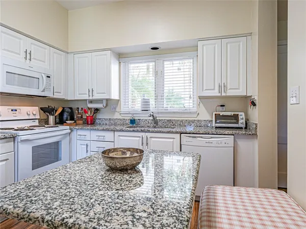 a kitchen with granite countertop a sink a stove a window and cabinets