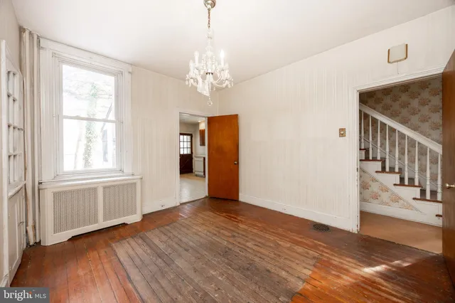 an empty room with wooden floor chandelier and windows