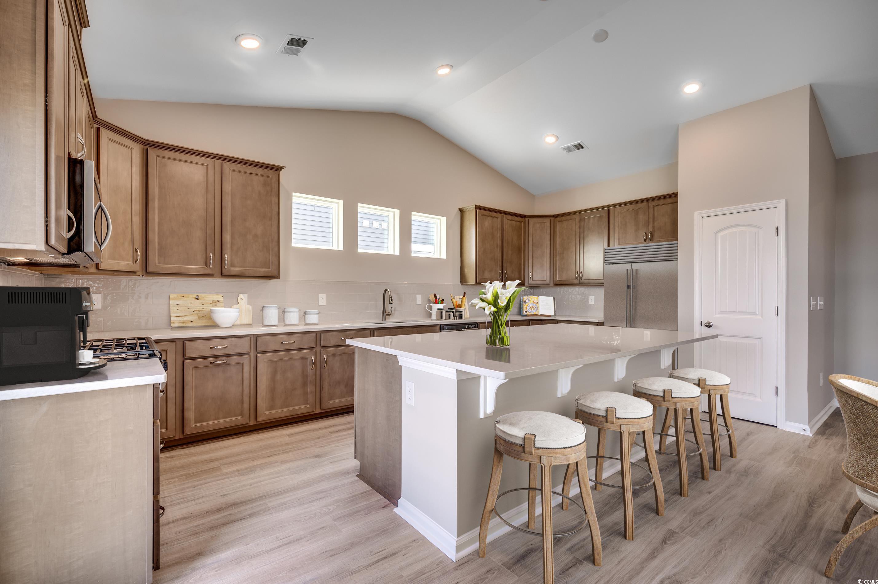 353 Kapalua Loop Little River, SC 29566 - Photo 6 of 11 Kitchen with a kitchen bar, a center island, vaulted ceiling, brown cabinetry, and appliances with stainless steel finishes