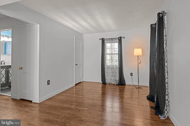 a view of an empty room with wooden floor and a bathroom