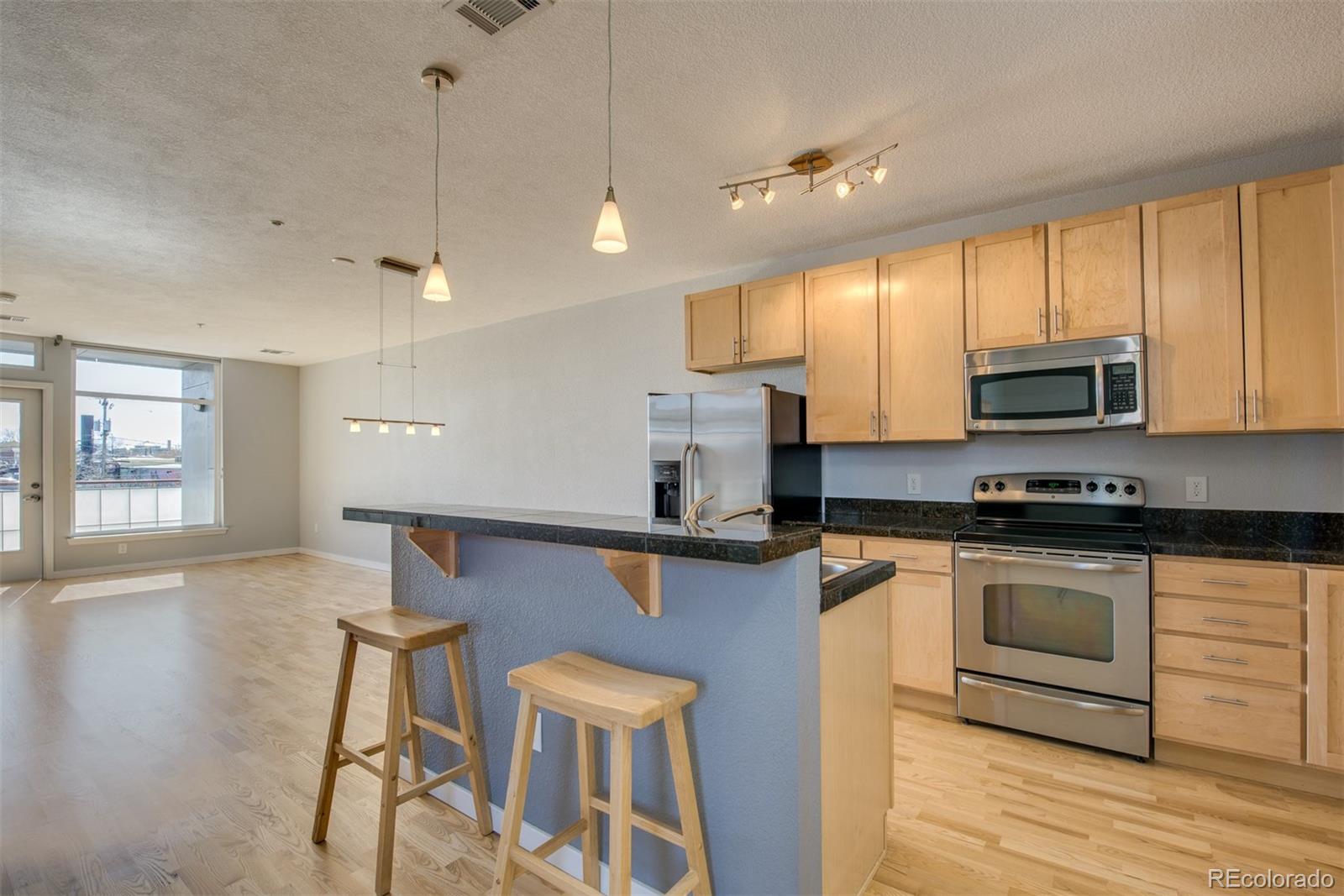 3101 Blake Street, Unit 308 Denver, CO 80205 - Photo 4 of 30 a kitchen with stainless steel appliances granite countertop a stove a sink a microwave a refrigerator white cabinets and wooden floor