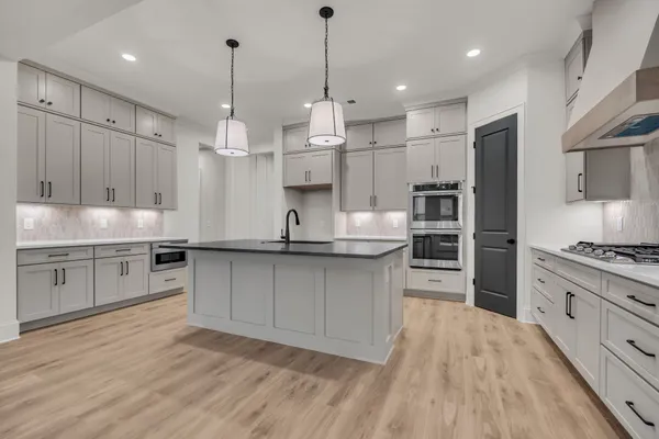 a large kitchen with granite countertop a stove a sink a refrigerator and white cabinets with wooden floor