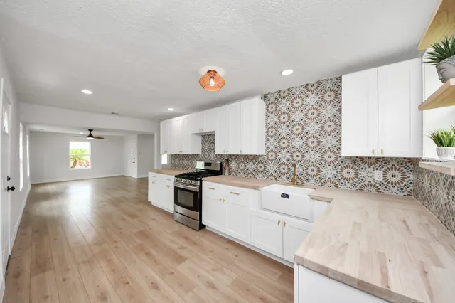 a kitchen with granite countertop a stove a sink and white cabinets with wooden floor