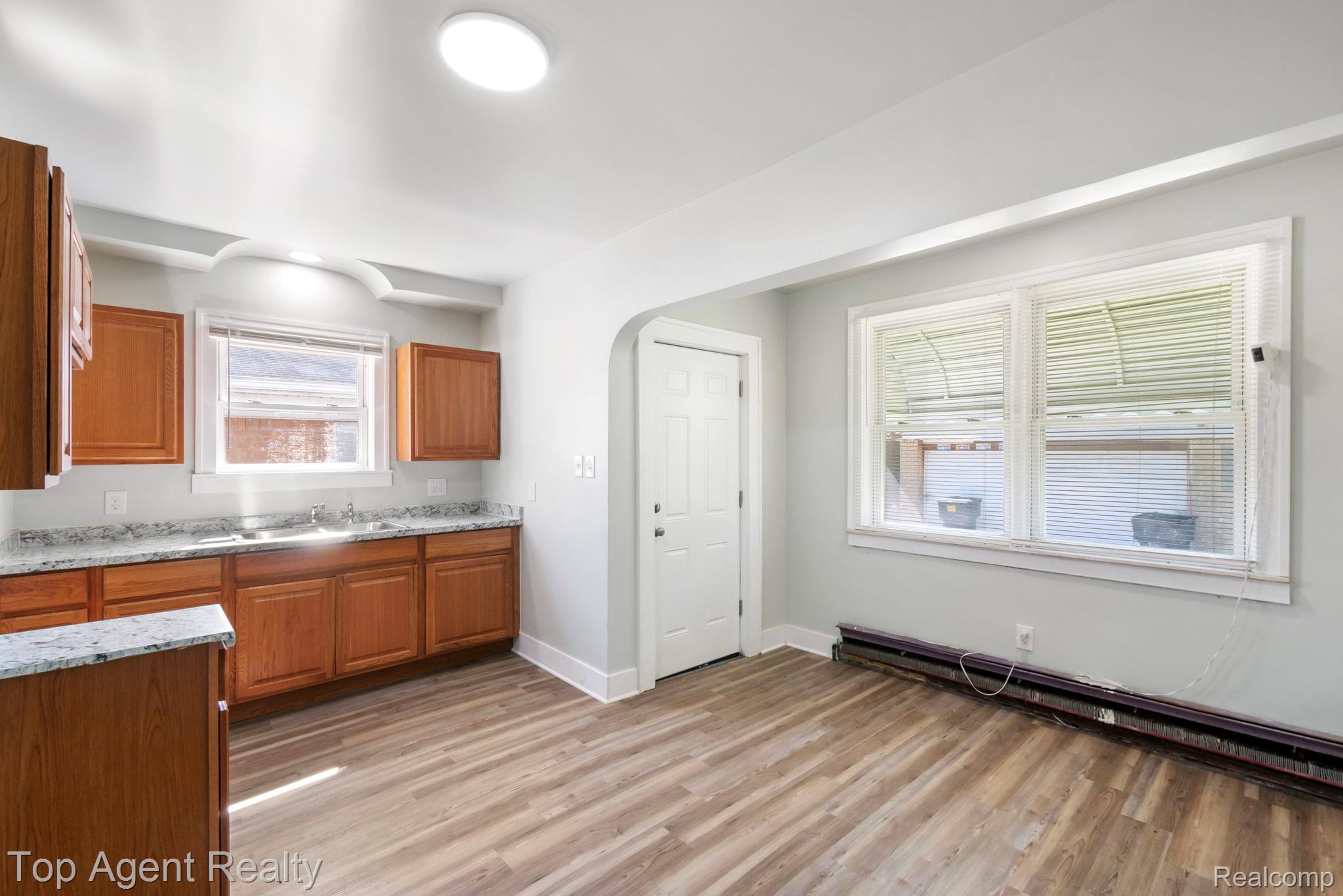 19217 Reno Street Detroit, MI 48205 - Photo 10 of 45 Kitchen featuring wood-finish flooring, wood cabinetry, stone-finish countertops, a double-basin sink, and a large window