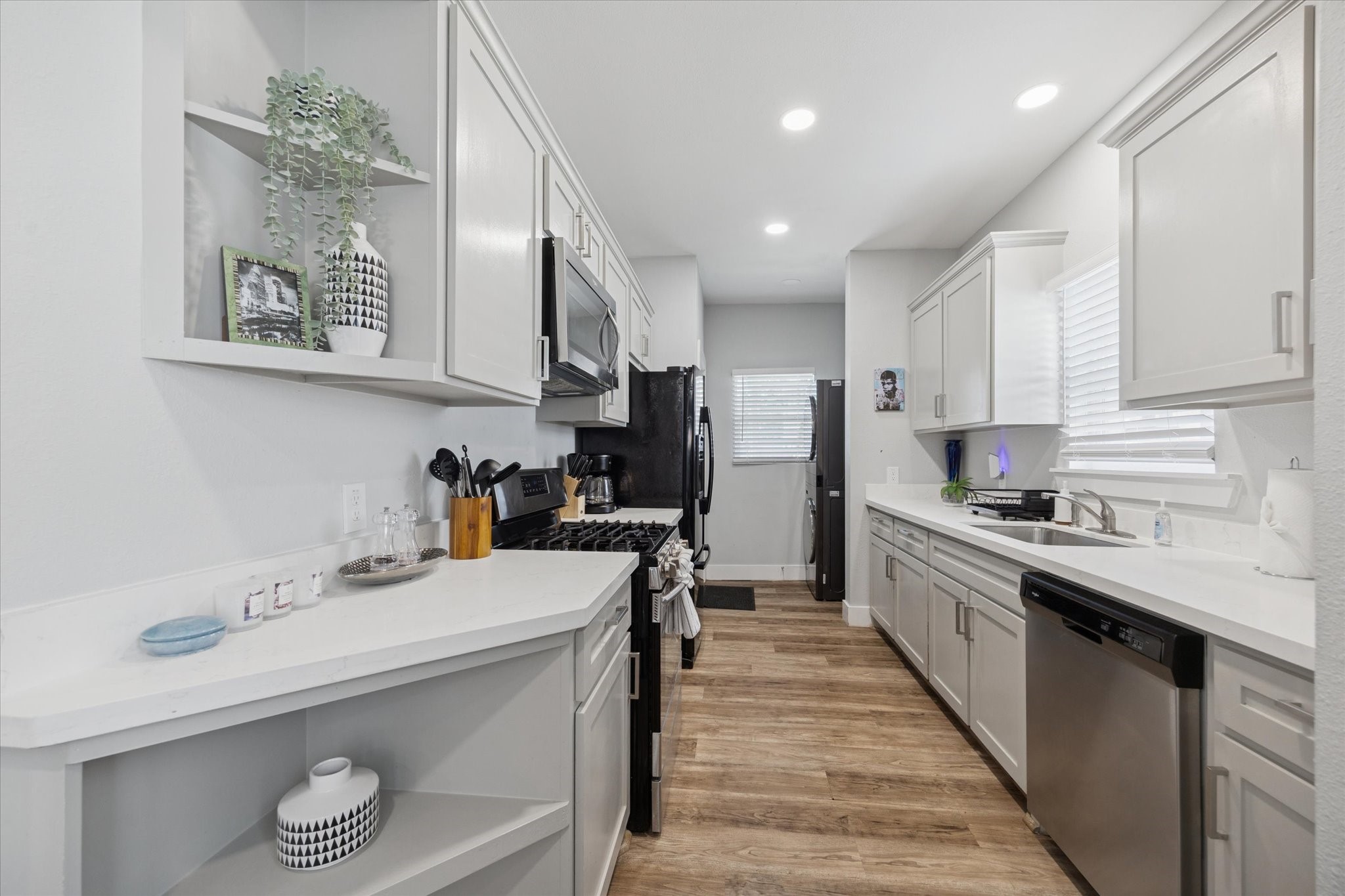 2410 Truxillo Street Houston, TX 77004 - Photo 8 of 41 Unit A (2-Bedroom): Updated galley-style kitchen showcasing quartz countertops, shaker cabinetry, stainless appliances, and convenient open shelving for added storage and display.