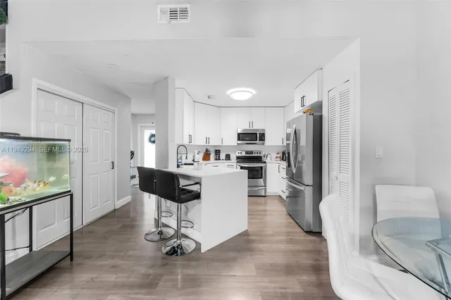 a kitchen with stainless steel appliances kitchen island granite countertop a refrigerator a stove a sink and white cabinets with wooden floor