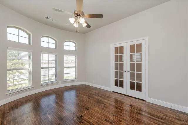 an empty room with wooden floor chandelier fan and windows