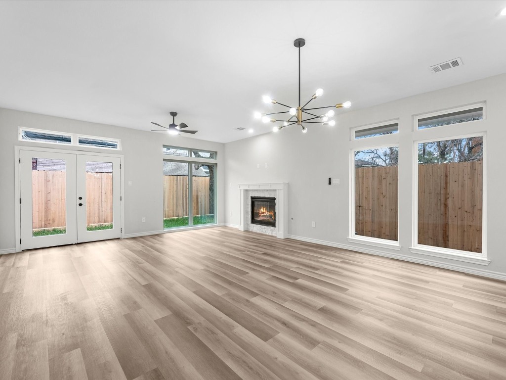 1319 West Bell Street Houston, TX 77019 - Photo 16 of 50 This spacious living room features large windows for natural light, a modern chandelier, ceiling fan, and a cozy fireplace. The light vinyl flooring and neutral walls create a warm, inviting atmosphere.