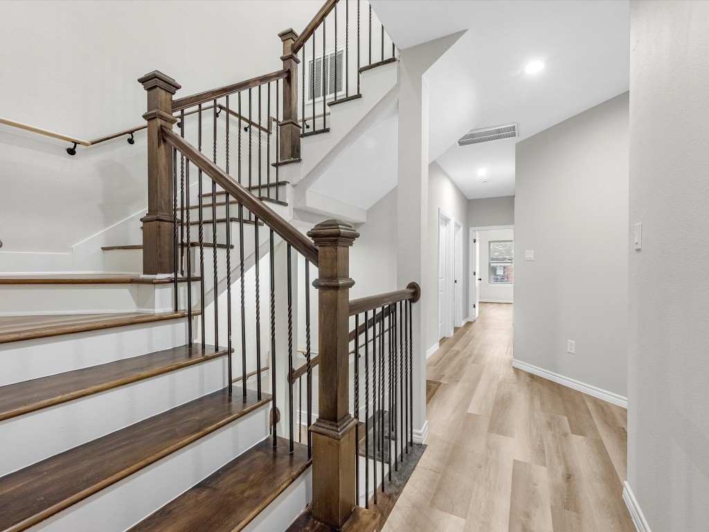 1319 West Bell Street Houston, TX 77019 - Photo 19 of 50 This photo showcases a modern, well-lit hallway with light vinyl flooring and a staircase featuring dark wood steps and elegant wrought iron railings. The space is bright, with clean white walls and recessed lighting, creating an open atmosphere.