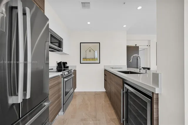 a living room with stainless steel appliances kitchen island granite countertop a sink a counter space and a view of living room