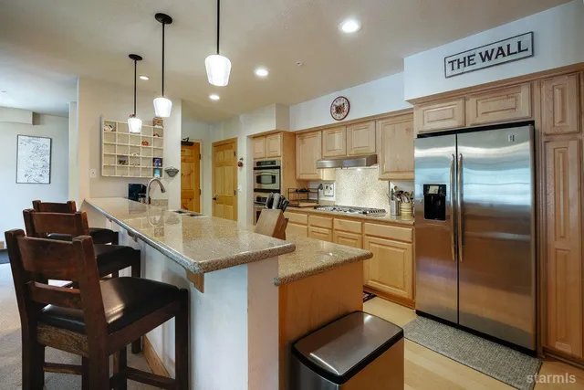 a kitchen with stainless steel appliances granite countertop a stove a refrigerator a oven a sink with island chairs and wooden cabinets