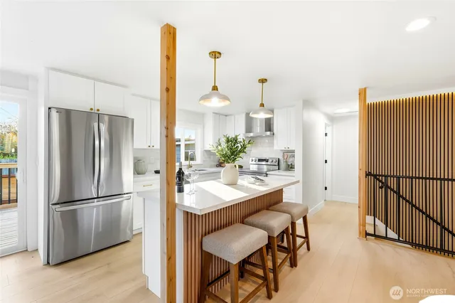 a kitchen with stainless steel appliances kitchen island granite countertop a refrigerator a stove and white cabinets with wooden floor