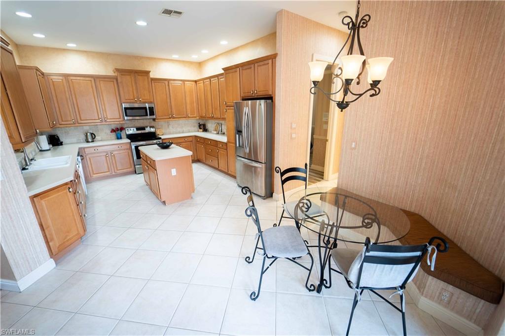 5886 Paradise Circle Naples, FL 34110 - Photo 5 of 19 Kitchen with pendant lighting, a chandelier, tasteful backsplash, a kitchen island, and appliances with stainless steel finishes