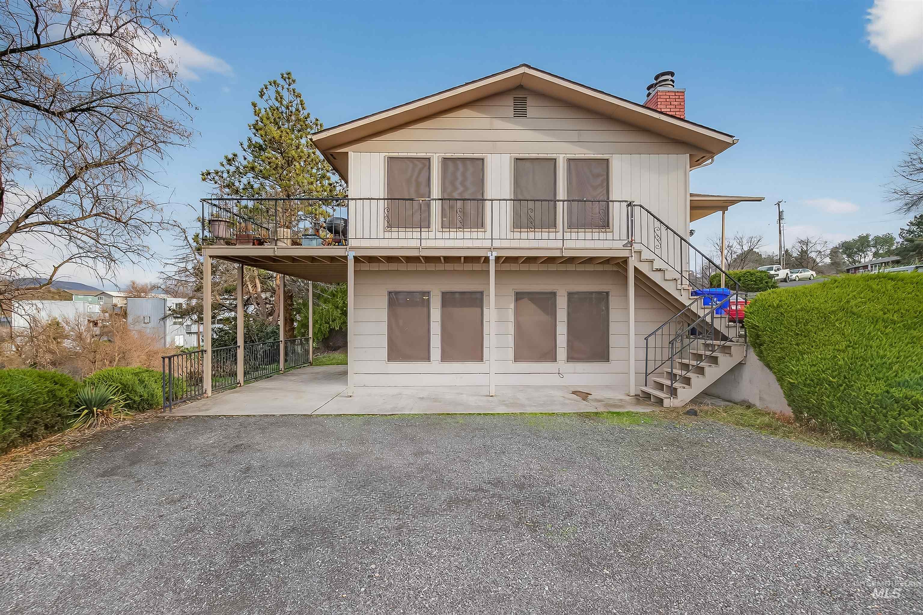 Back of house with stairs, a patio, a chimney, a balcony, and driveway