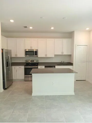 a large kitchen with stainless steel appliances granite countertop a stove a refrigerator a sink and white cabinets