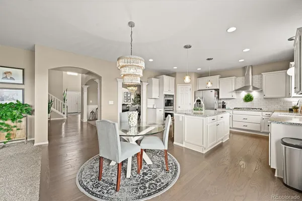a kitchen with stainless steel appliances kitchen island granite countertop a dining table chairs and white cabinets