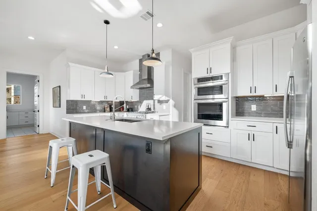 a kitchen with stainless steel appliances kitchen island granite countertop a sink a stove a refrigerator and white cabinets with wooden floor