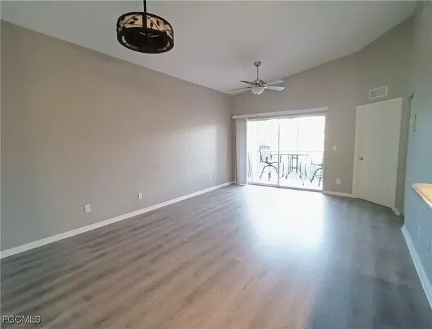 an empty room with wooden floor chandelier fan and windows