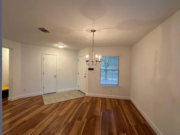 an empty room with wooden floor chandelier and windows
