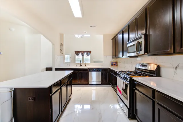 a kitchen with stainless steel appliances granite countertop a sink a stove top oven a refrigerator with wooden floors