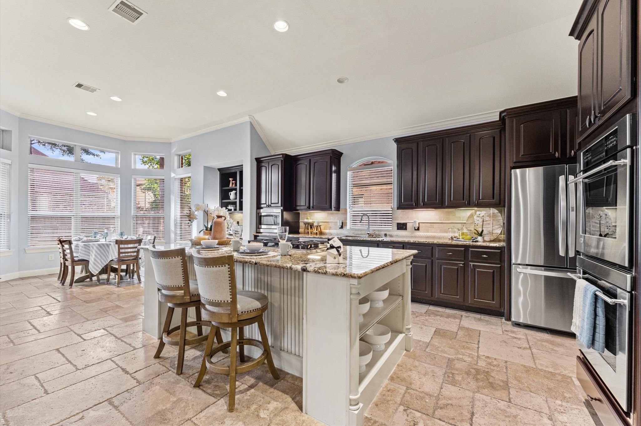 70 Valera Ridge Drive Spring, TX 77389 - Photo 14 of 37 This spacious kitchen features dark wood cabinets, stainless steel appliances, and a large central island with granite countertops. The adjacent dining area is bright with large windows, and the tile flooring adds a touch of elegance.