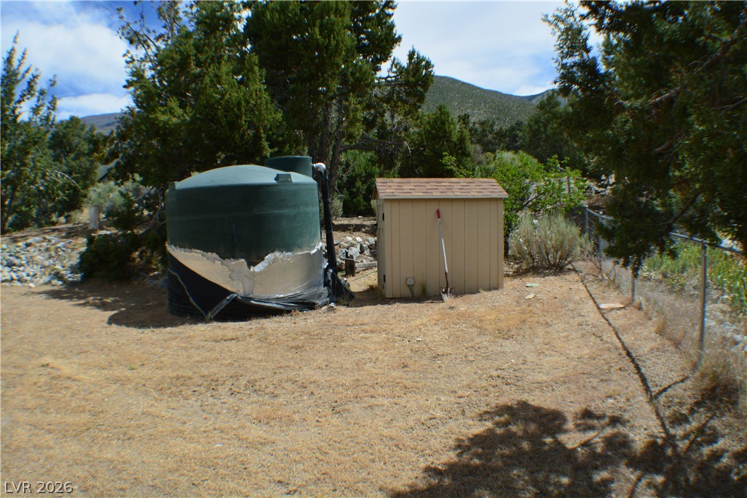 1321 Trout Canyon Road Las Vegas, NV 89124 - Photo 48 of 50 A utilitarian shed and water tank reside within a fenced yard, backed by trees and distant mountains.