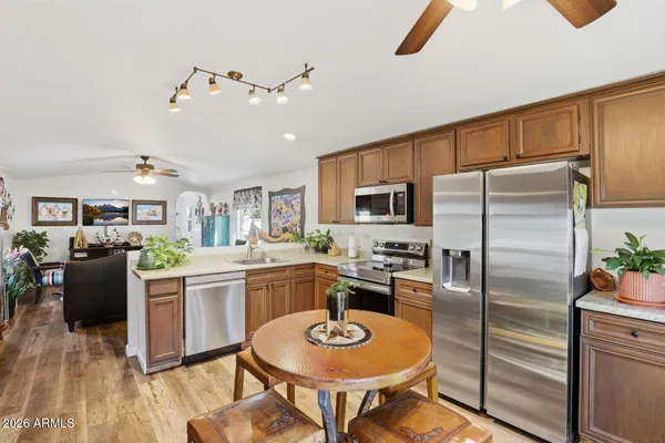 a kitchen with stainless steel appliances kitchen island granite countertop a refrigerator a stove a sink a dining table and chairs with wooden floor