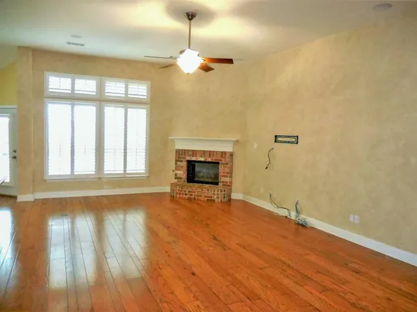 an empty room with wooden floor fireplace and windows