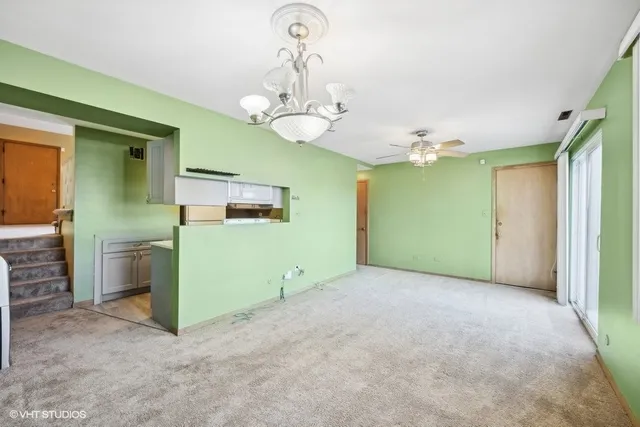 en empty room with a chandelier fan and kitchen view