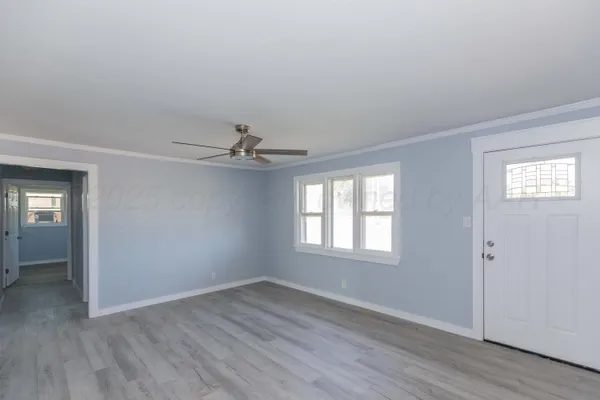 an empty room with wooden floor chandelier fan and windows