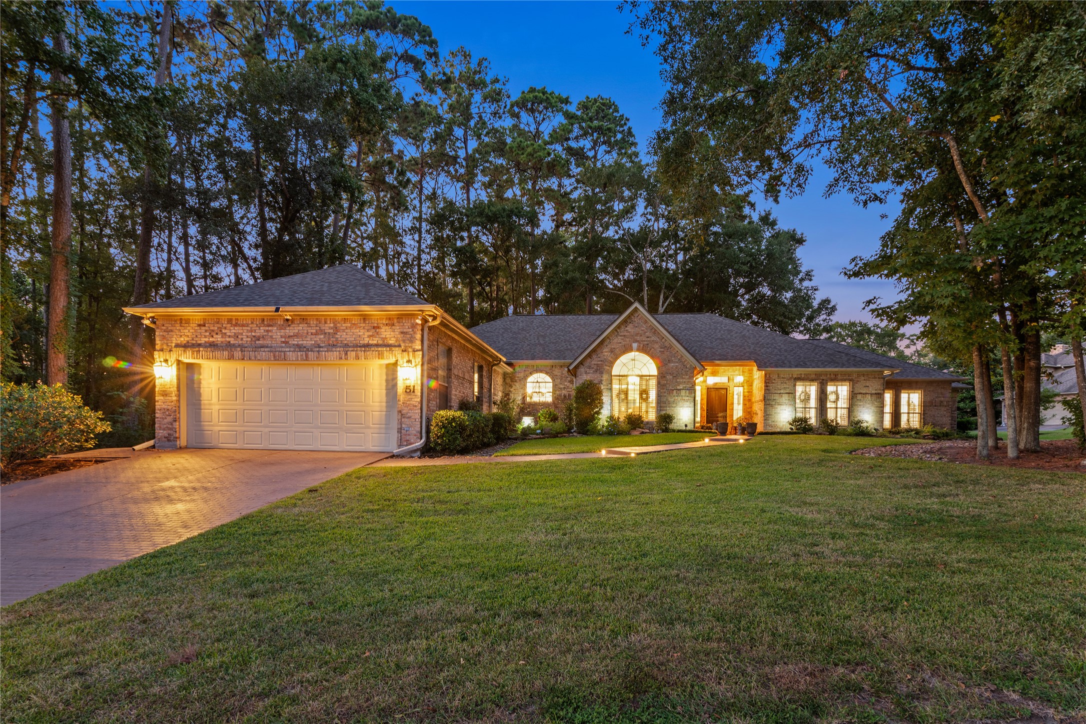 901 Longmire Road, Unit 51 Conroe, TX 77304 - Photo 48 of 48 Built to please with large rooms, great split floor plan with two primary bedrooms with sitting area and lots of room for privacy in this single-story brick home nestled among mature trees, featuring a spacious front yard and oversized lot and half with an inviting pathway, and warm exterior lighting for a welcoming ambiance.