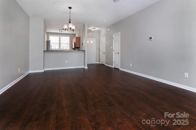 an empty room with wooden floor chandelier and windows