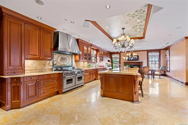 a large kitchen with a large counter space a chandelier stainless steel appliances and cabinets