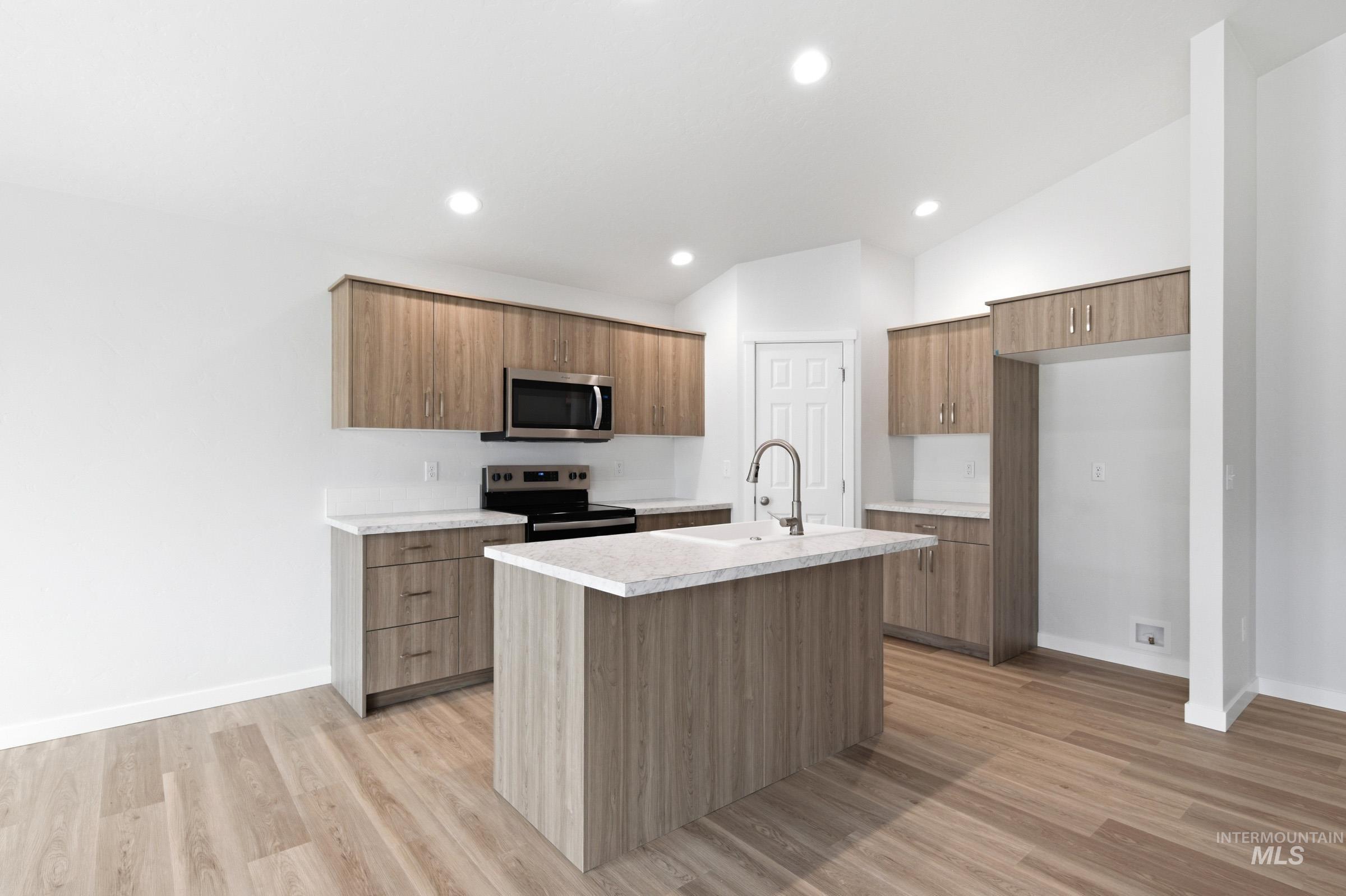 13735 Inman Court Caldwell, ID 83607 - Photo 5 of 20 Kitchen featuring light countertops, stainless steel appliances, a kitchen island with sink, wood finish cabinets, and vaulted ceiling