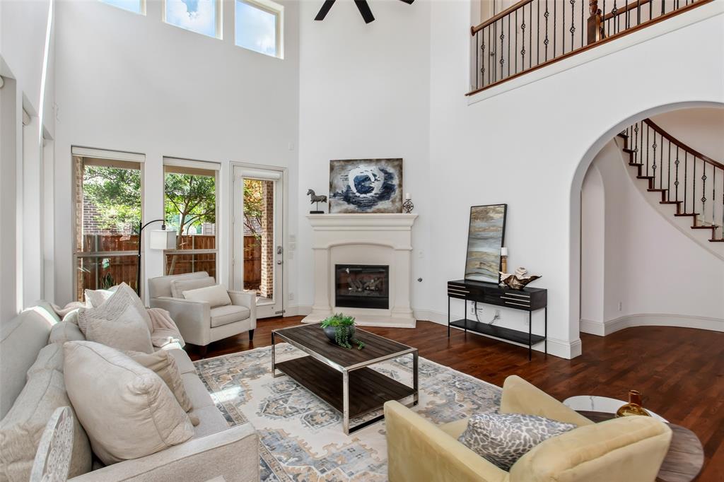 846 Deerfield Road Allen, TX 75013 - Photo 8 of 40 Two-story living area featuring a fireplace with a stone surround, rich wood-finish flooring, a wrought iron staircase, high ceilings, and multiple windows