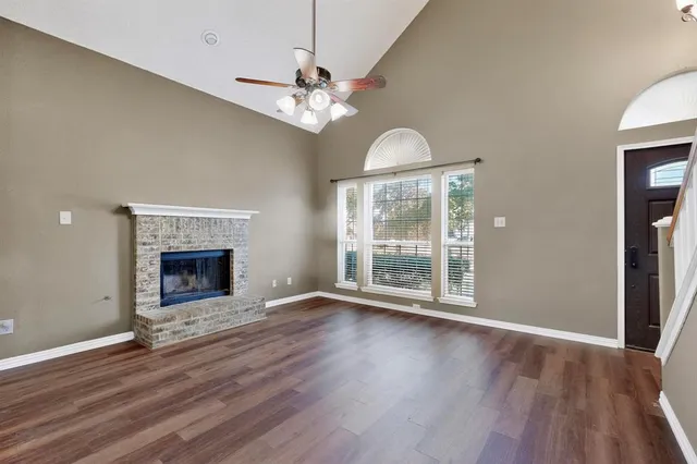 a view of an empty room with wooden floor fireplace and a window