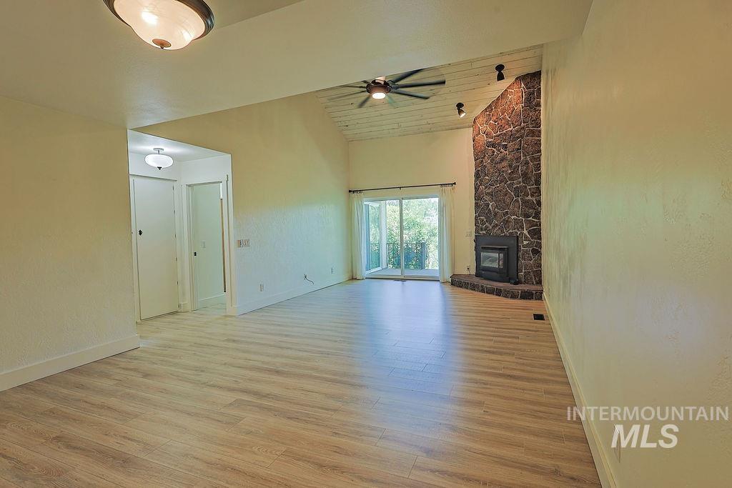 640 Morrison Street Twin Falls, ID 83301 - Photo 14 of 30 Spacious living area featuring wood-finish flooring, a stone fireplace with hearth, a vaulted ceiling with exposed beams, track lighting, and sliding glass doors opening to the exterior