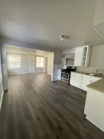a view of a kitchen and an empty room with wooden floor and a window