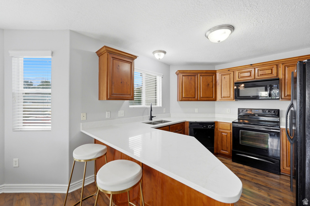 116 East Resaca Drive, Unit F6 Sandy, UT 84070 - Photo 11 of 32 Kitchen featuring a peninsula with a white countertop, wood-finish cabinetry, black appliances, a double basin sink with a matte black faucet, and hard surface flooring