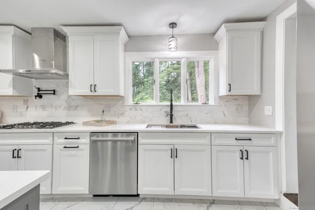 a kitchen with white cabinets appliances a sink and a window