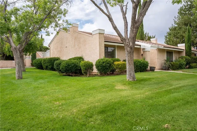 a view of a white house next to a yard with a large tree