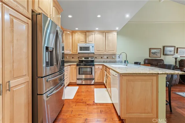 a kitchen with stainless steel appliances granite countertop a refrigerator a sink dishwasher and a stove with wooden floor