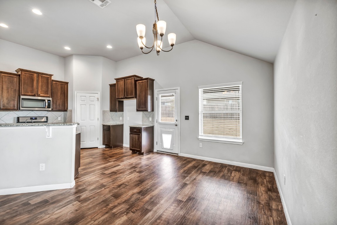 539 Merlin Lane Leander, TX 78641 - Photo 7 of 18 Kitchen with dark brown cabinets, light stone counters, decorative backsplash, a chandelier, and hanging light fixtures