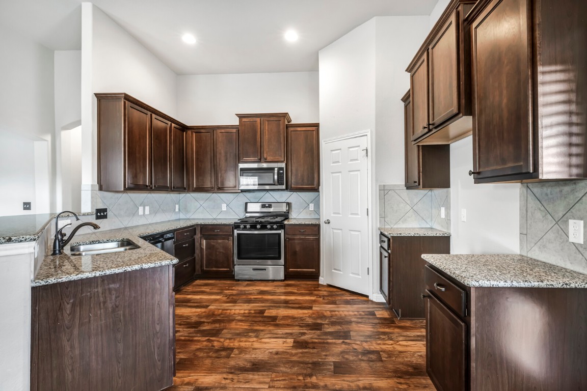 539 Merlin Lane Leander, TX 78641 - Photo 8 of 18 Kitchen featuring light stone countertops, stainless steel appliances, dark brown cabinetry, decorative backsplash, and dark wood-style flooring