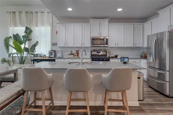 a kitchen with stainless steel appliances granite countertop a stove a sink a microwave a refrigerator and white cabinets