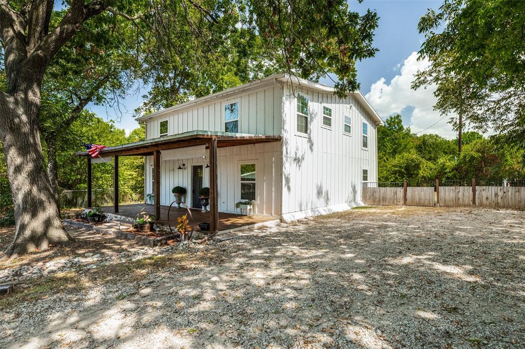 5455-924 County Road Nevada, TX 75173 - Photo 2 of 14 White board and batten exterior, covered wooden porch, gravel parking area, and a wooden privacy fence