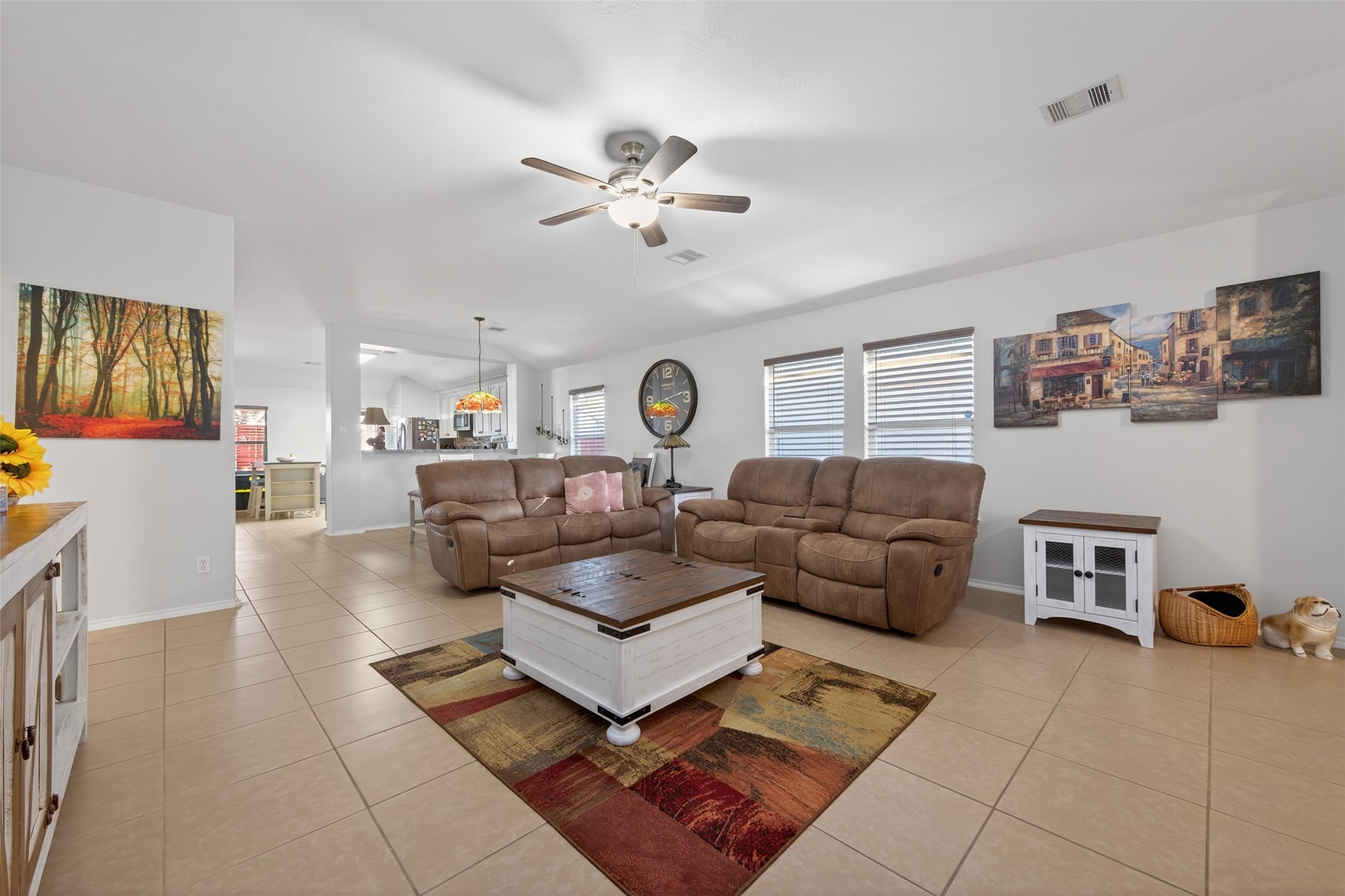 20218 Appaloosa Ridge Drive Humble, TX 77338 - Photo 11 of 44 Bright, spacious living area with neutral tile flooring and cozy seating. Features a ceiling fan, large windows for natural light, and an open layout leading to the kitchen. Decor includes wall art and a functional coffee table, creating a welcoming atmosphere.
