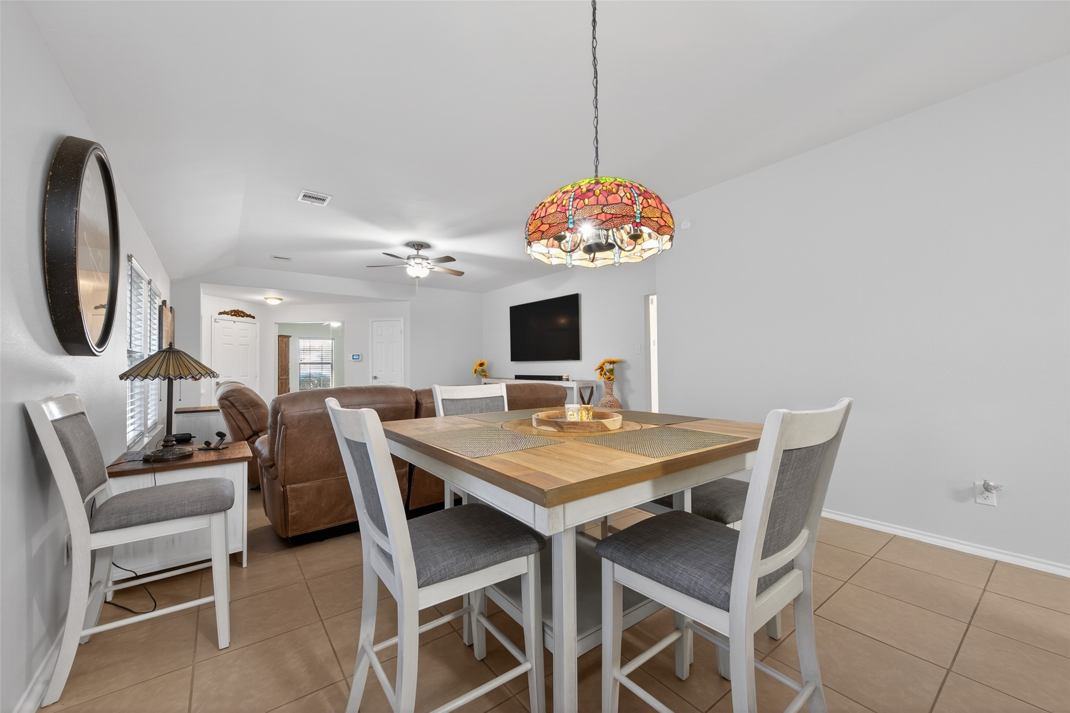 20218 Appaloosa Ridge Drive Humble, TX 77338 - Photo 15 of 44 This photo shows a bright, open-concept living and dining area with neutral tile flooring. The space features a modern ceiling fan, a colorful pendant light over the dining table, and a wall-mounted TV. Cozy seating and ample natural light create a welcoming atmosphere.