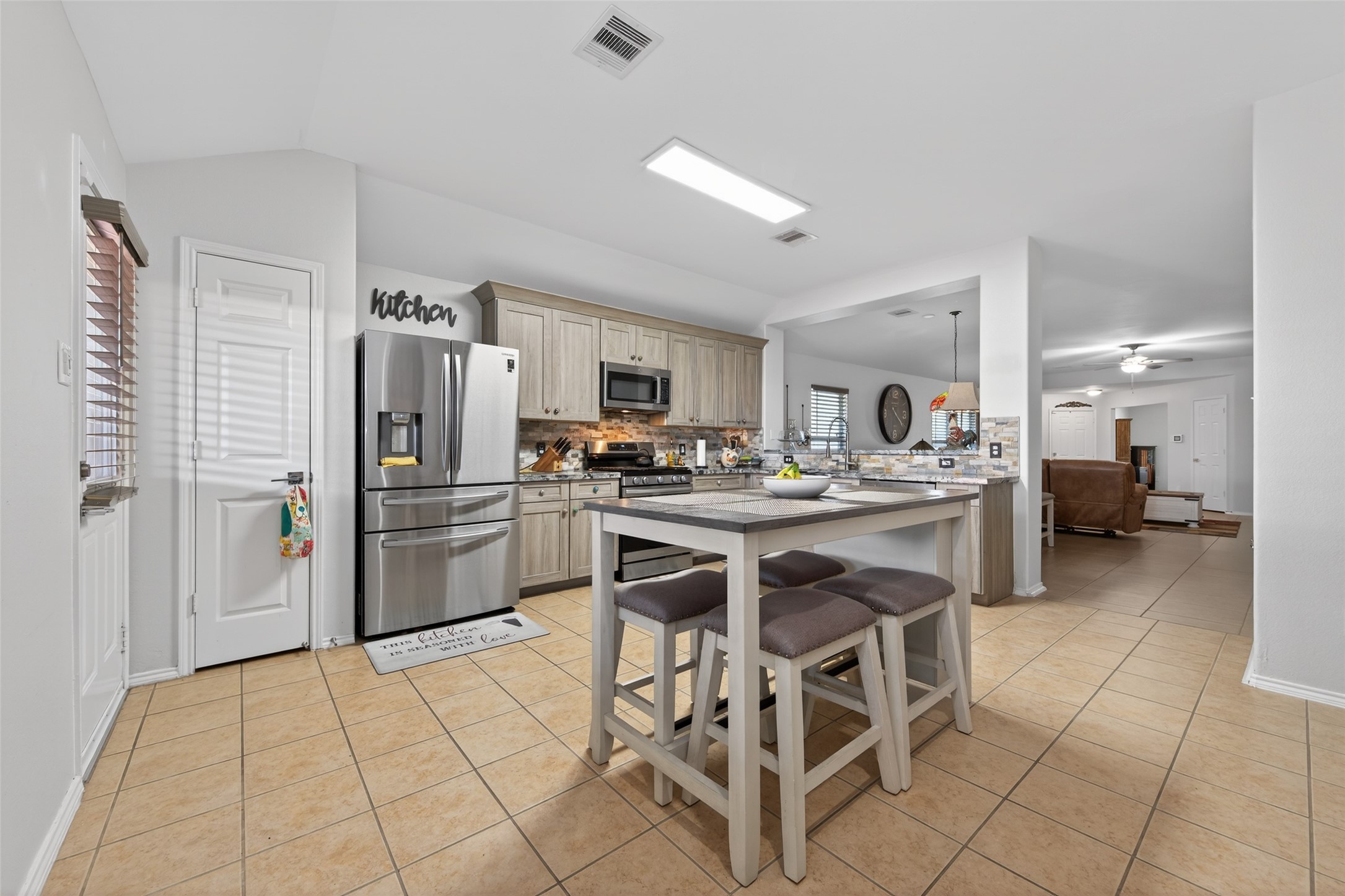 20218 Appaloosa Ridge Drive Humble, TX 77338 - Photo 20 of 44 This photo showcases a modern kitchen with stainless steel appliances, including a large refrigerator. It features a central island with seating, light wood cabinetry, and a tile floor. The space is open and bright, connecting to a living area, creating a spacious and inviting atmosphere.