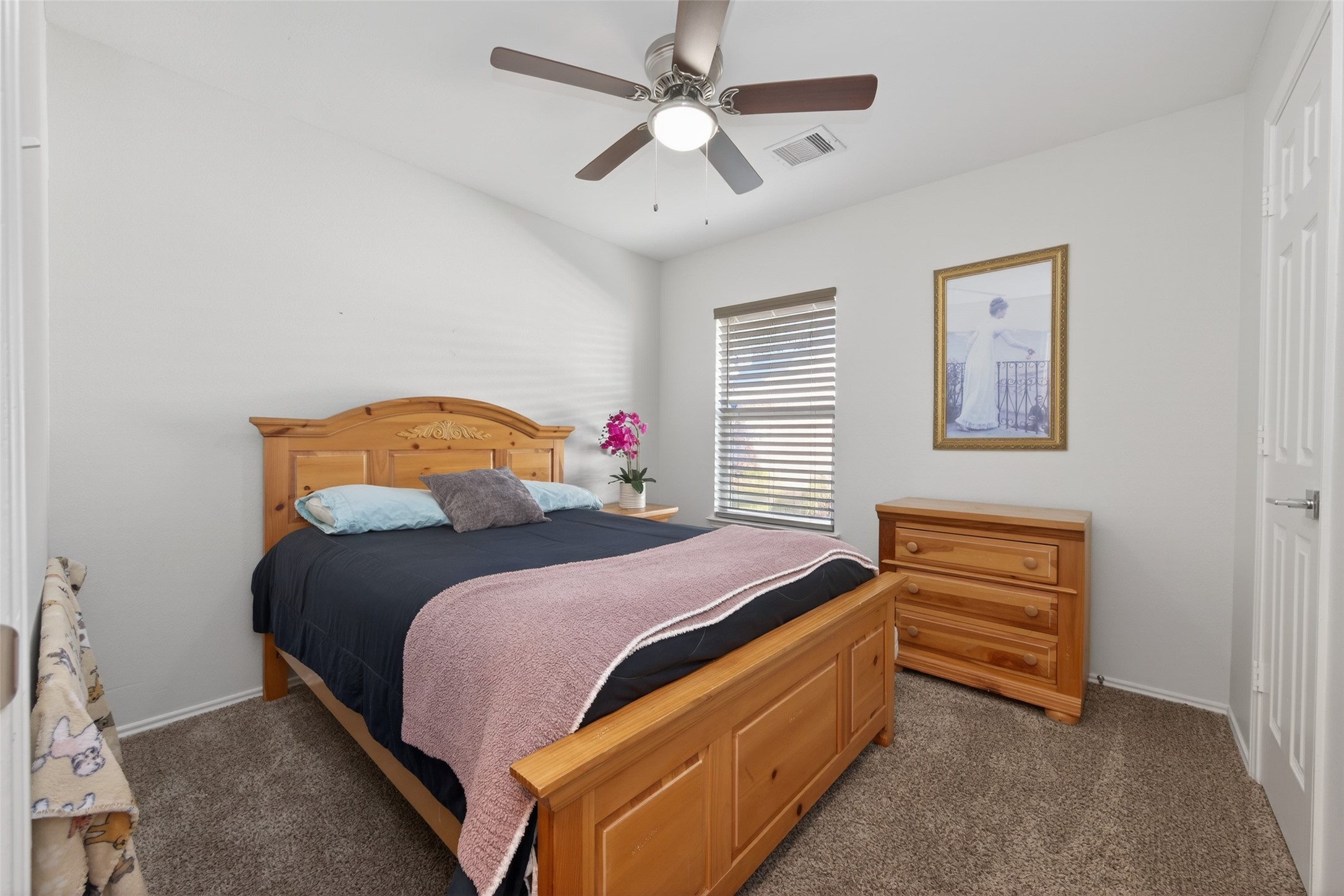 20218 Appaloosa Ridge Drive Humble, TX 77338 - Photo 26 of 44 This cozy bedroom features a wooden bed and dresser set, a ceiling fan, and a window with blinds. The neutral walls and carpet create a warm atmosphere, complemented by a decorative wall picture and a touch of color from a flower arrangement.